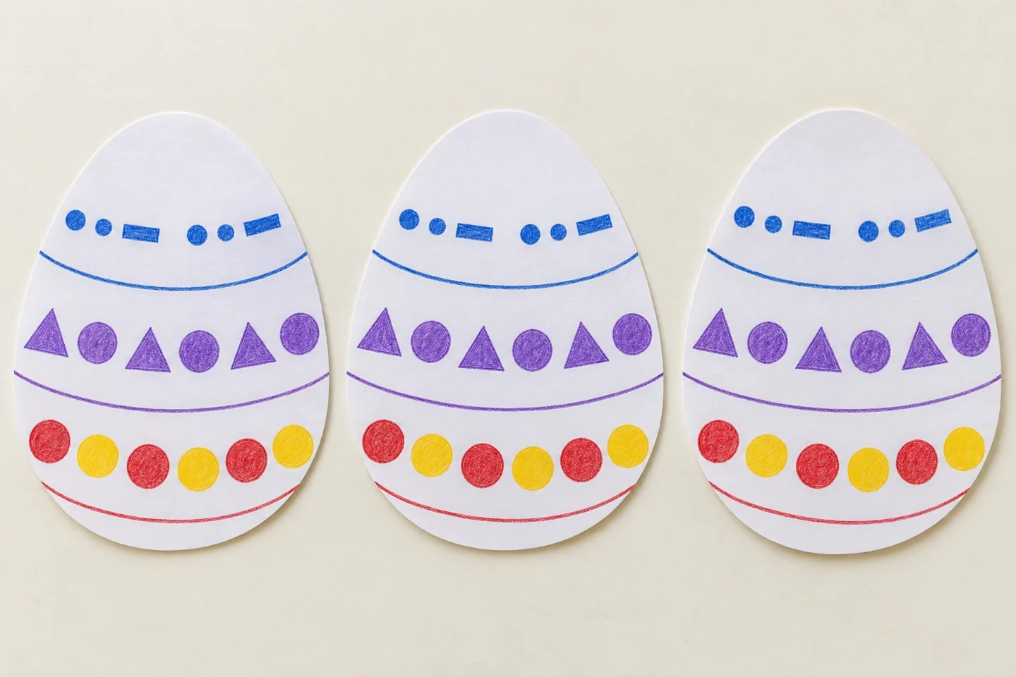 Overhead detail of three decorated paper egg cutouts, each with three curved bands and clearly repeated units