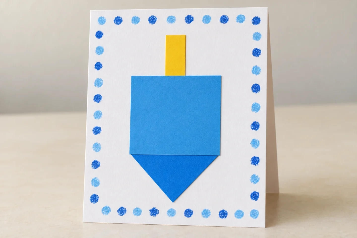 One finished folded card with large unlettered blue dreidel, yellow handle and white dotted border; no readable generated greeting
