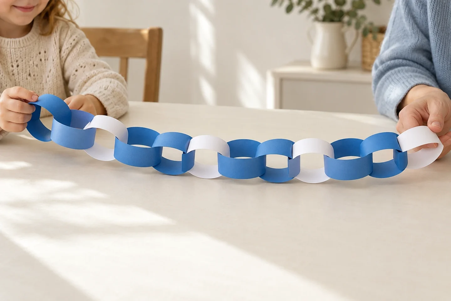 A child and adult holding a blue-blue-white paper chain