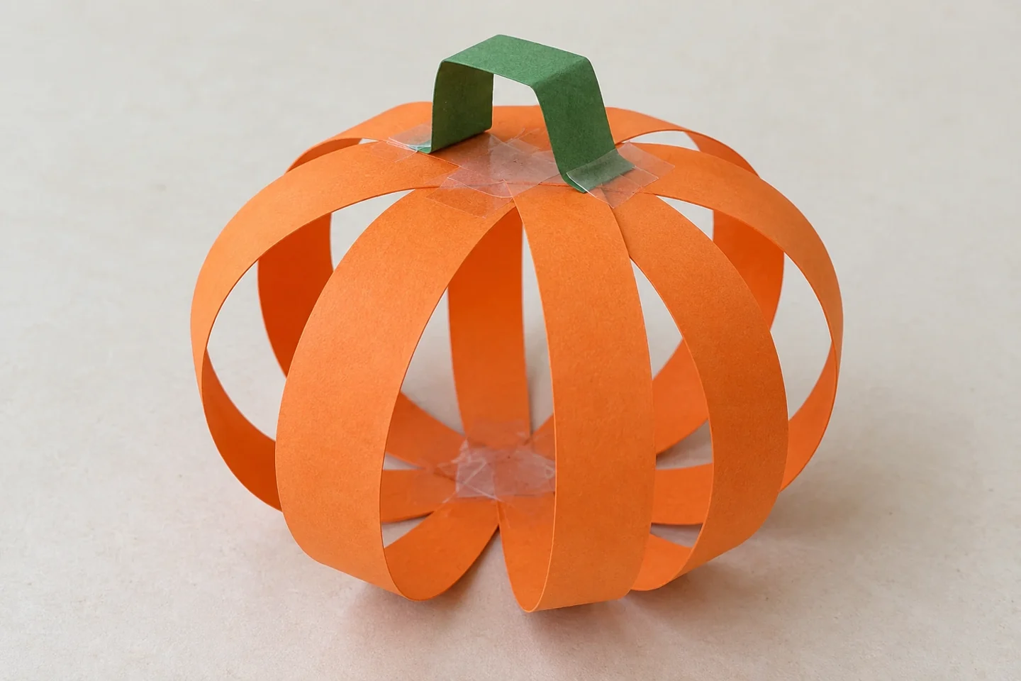 Finished open orange pumpkin with eight curved ribs and a folded green bridge-shaped stem.