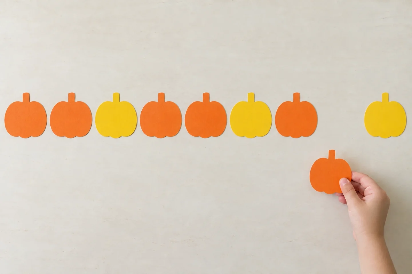 A child chooses an orange pumpkin to fill the gap in an orange-orange-yellow pattern.